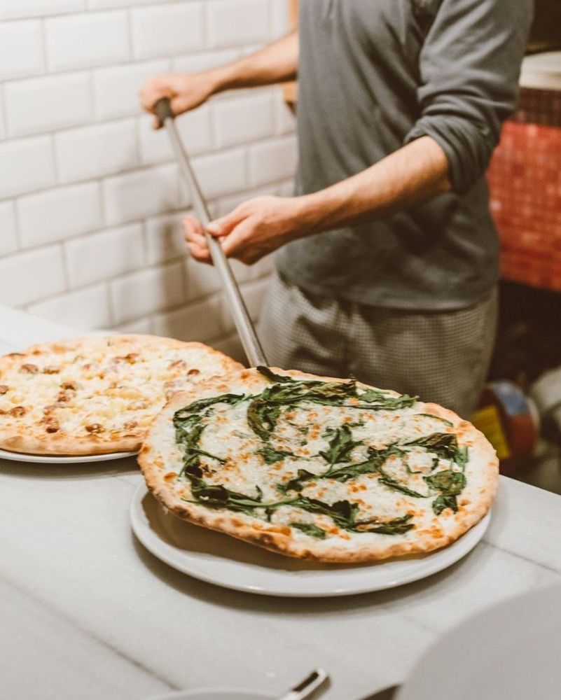 Pizzaiolo di spalle che inforna con la pala